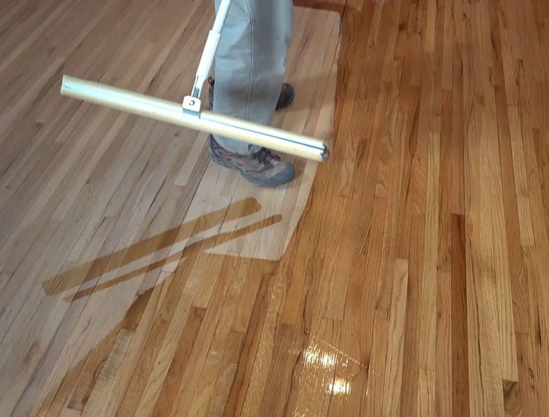 A worker laying down a fresh coat of floor finish with an applicator during a scrub and recoat.