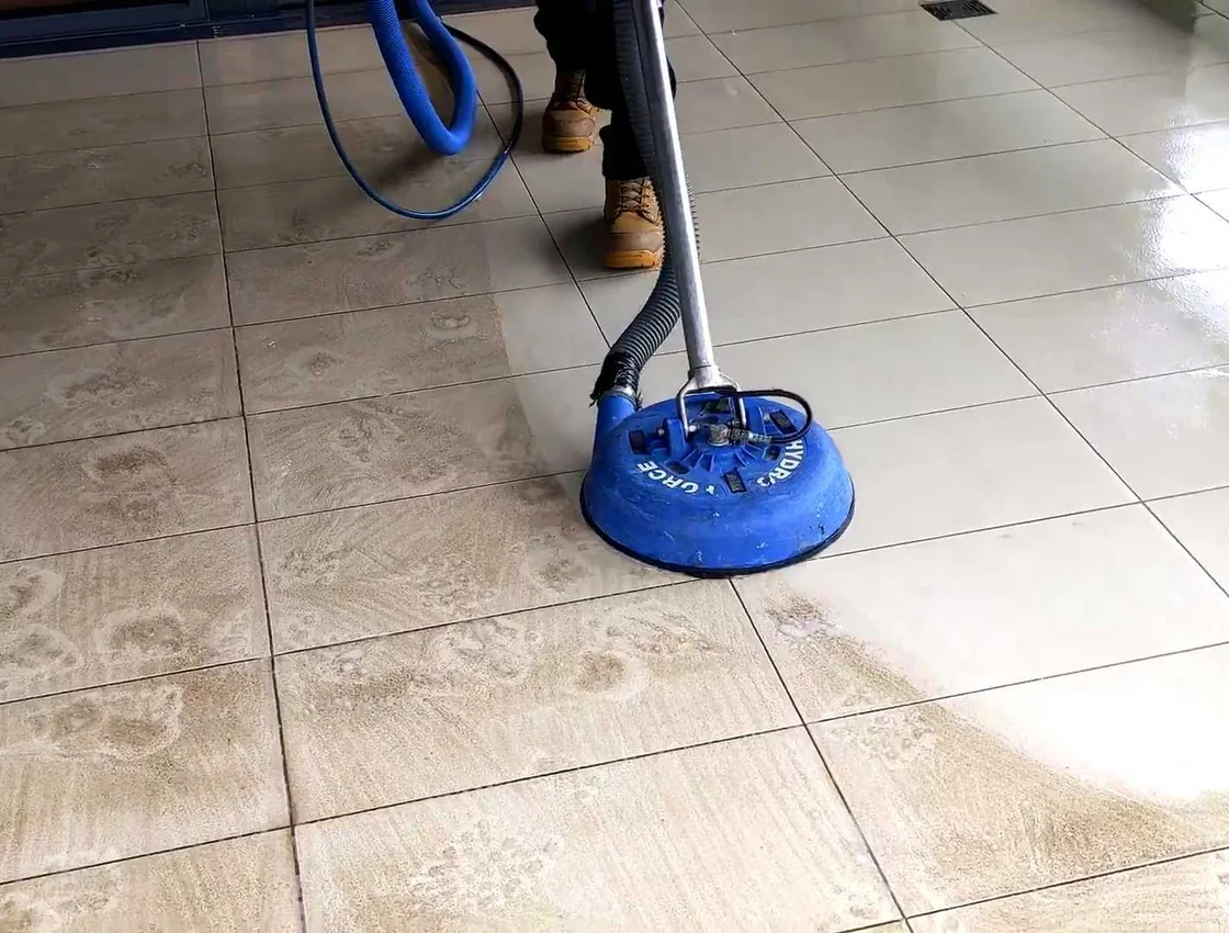 A tile and grout cleaning tool restoring a grimy tile floor, with a clear line between the dirty and freshly cleaned areas.